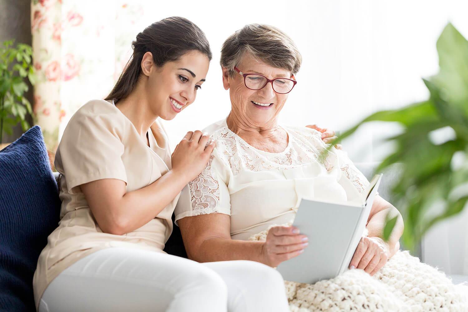 Senior woman and nurse reading together on a sofa