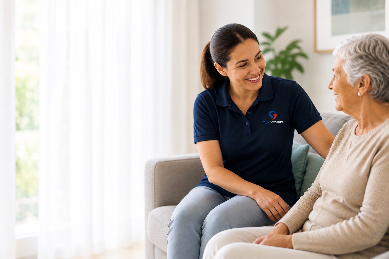 Smiling True Path Care support worker with an elderly woman on a sofa