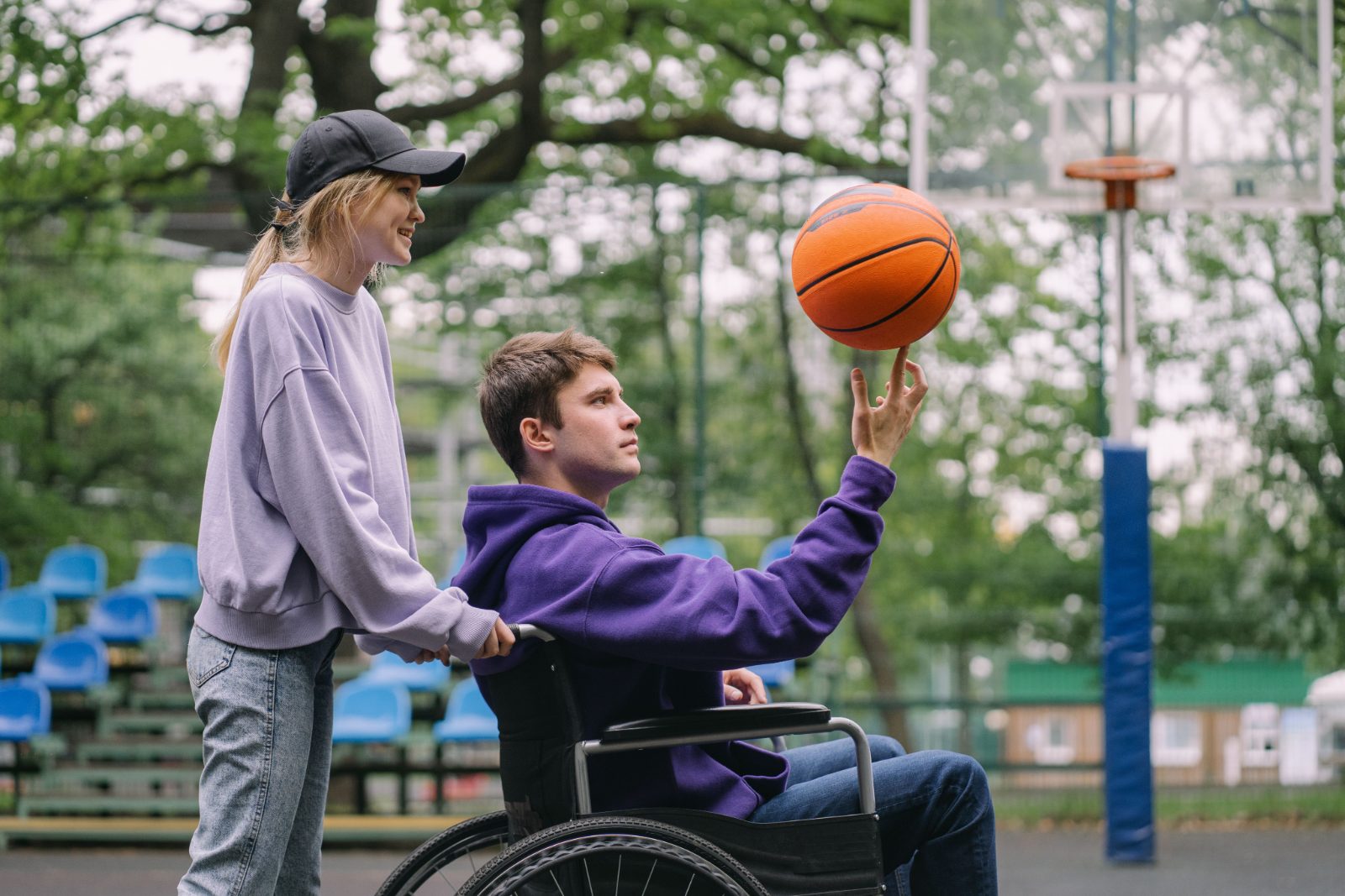Young man in a wheelchair spinning a basketball with a friend