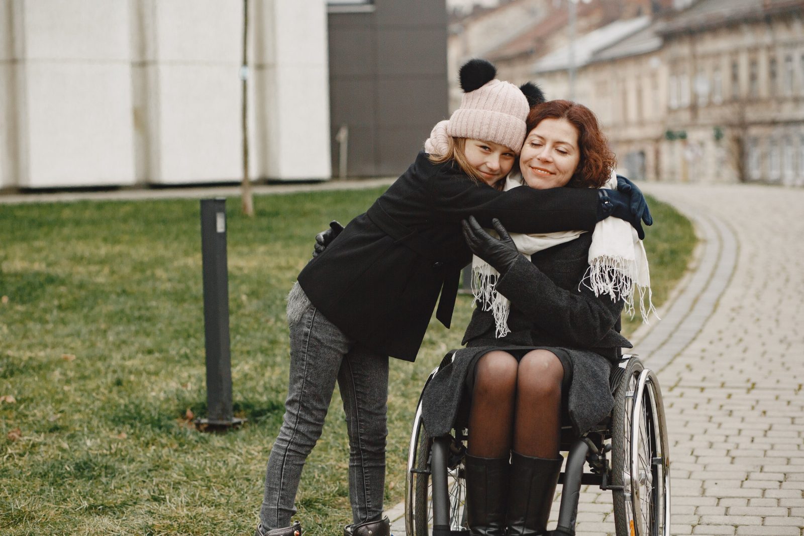 Woman hugging a young woman in a wheelchair outdoors